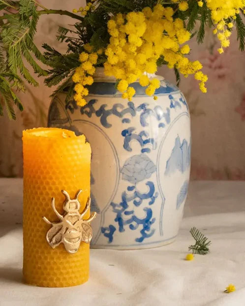 Honeycomb-textured beeswax candle with a brass bee on the front, styled beside a blue and white ginger jar and yellow candle