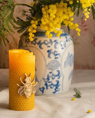 Honeycomb-textured beeswax candle with a brass bee on the front, styled beside a blue and white ginger jar and yellow candle
