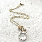 Gold necklace layering a faceted clear crystal pendant, a starburst charm, and a small pavé bead.