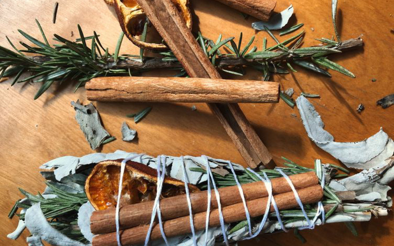 Handcrafted sage smudge bundle with cinnamon sticks, rosemary, eucalyptus, and dried citrus styled in an elevated bohemian wellness aesthetic.